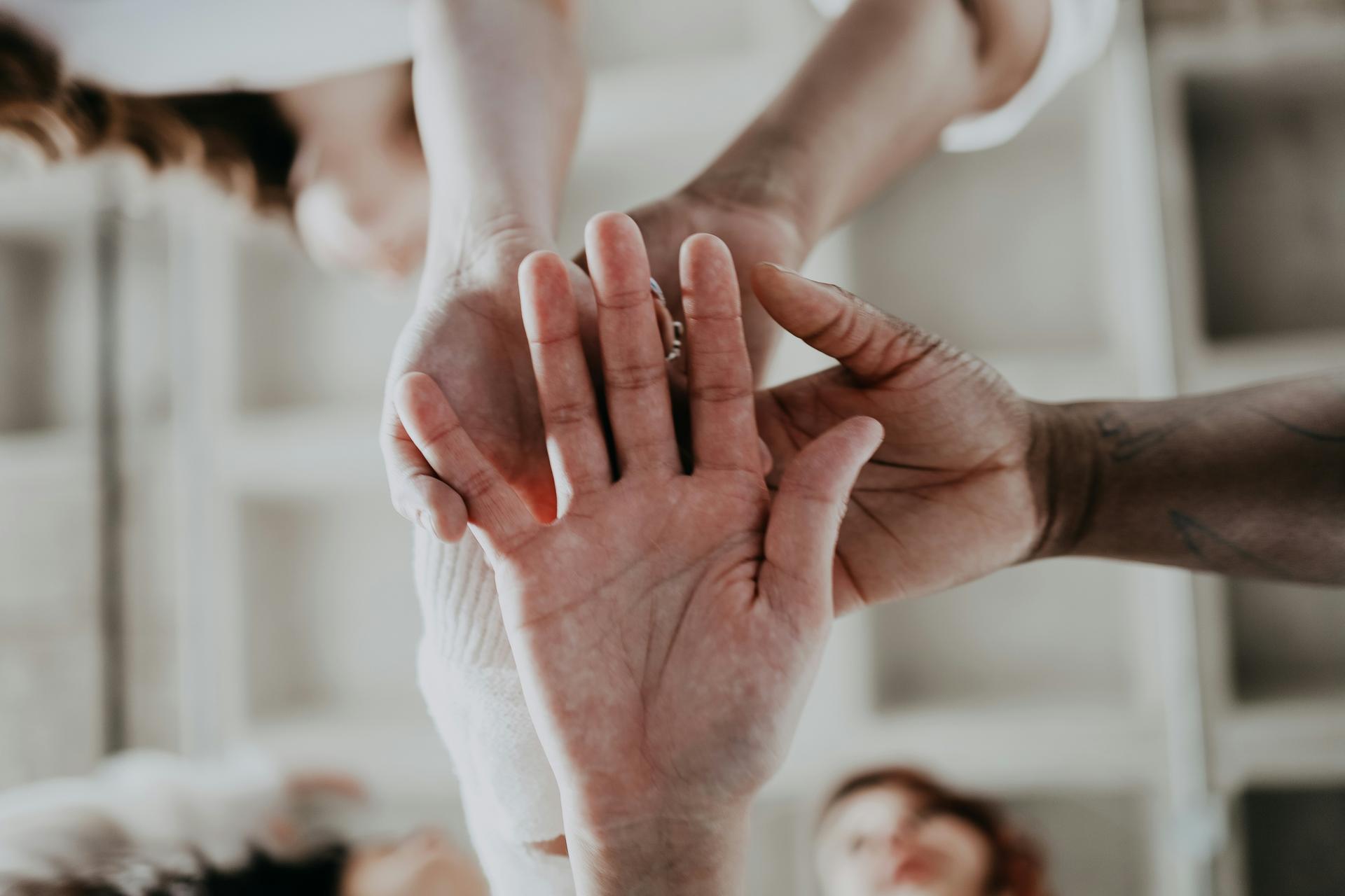 Close-up of four people's hands stacked on top of one another, with blurred figures in the background.